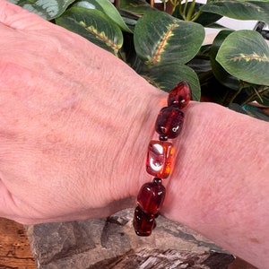 May include: A bracelet featuring rectangular amber beads in shades of brown and orange. The beads are strung together, creating a striking accessory. The bracelet is worn on a wrist.