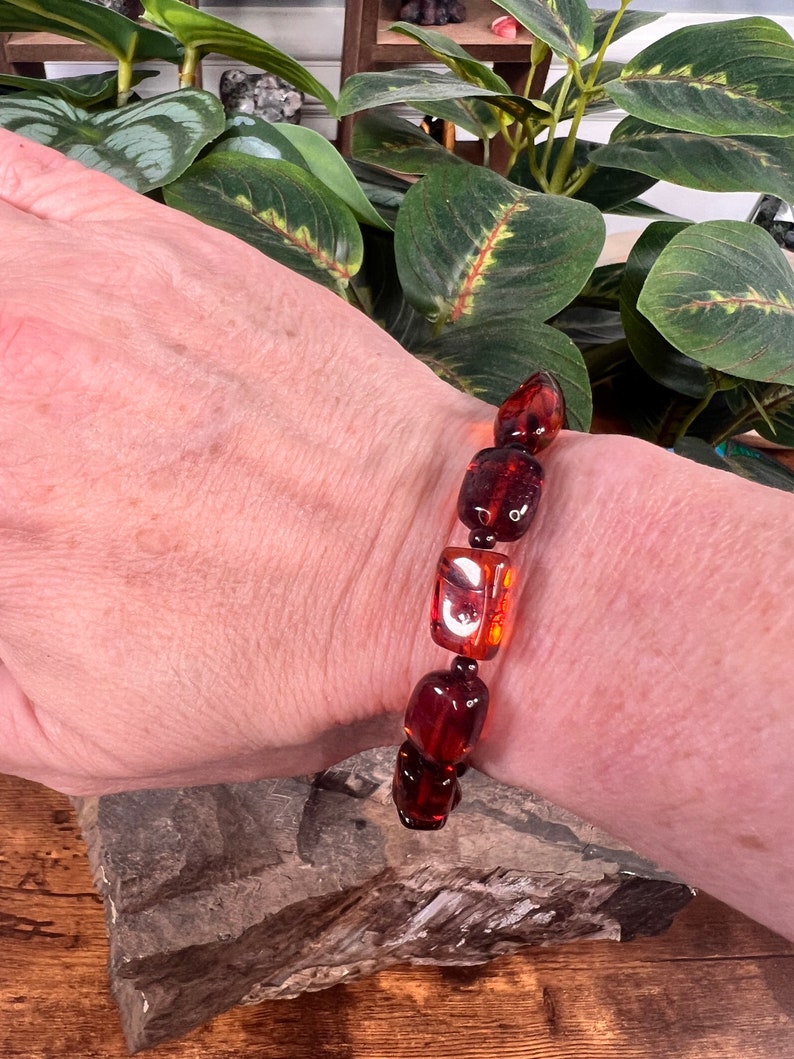 May include: A bracelet featuring rectangular amber beads in shades of brown and orange. The beads are strung together, creating a striking accessory. The bracelet is worn on a wrist.