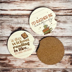 May include: Two round, white ceramic coasters with brown text and illustrations. One coaster features the text "I'd rather be reading" with a stack of books and a cup of coffee. The other coaster features the text "a day without reading is like... JUST KIDDING. I HAVE NO IDEA".