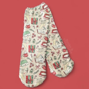 May include: Cream-colored scarf with a repeating pattern of books, gifts, mugs, stockings, and candy canes in red, green, and white. The scarf has a soft, fuzzy texture and a red background.