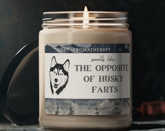 May include: A soy wax candle in a clear glass jar with a black label that reads "HUSKY AROMATHERAPY Soy Wax Blend 9oz smells like... THE OPPOSITE OF HUSKY FARTS Infused with unconventional blends of massive amounts of dog treats, and a hint of best dog food."