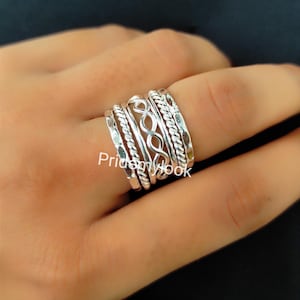 Peut inclure: Un ensemble de cinq bagues empilables en argent avec différentes textures et motifs. Les bagues sont portées sur un doigt.