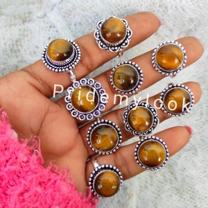 May include: A collection of silver-toned rings with large, round tiger's eye stones. The rings feature ornate, detailed settings. The tiger's eye stones display a warm, golden-brown color with natural patterns. The rings are displayed on a hand.
