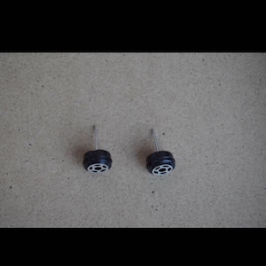 May include: A pair of silver stud earrings with black tire-shaped charms. The charms have a silver rim and a black center.