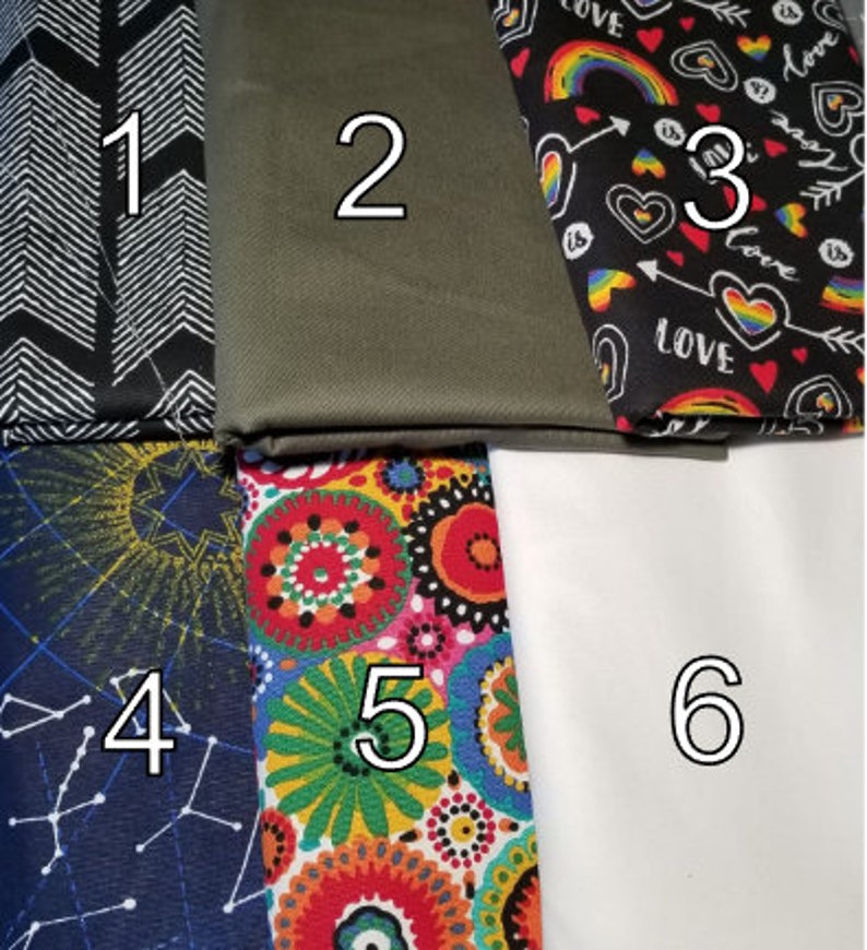 May include: Six fabric swatches with numbers 1 through 6.  Swatch 1 is black with white chevron arrows. Swatch 2 is olive green. Swatch 3 is black with rainbow, hearts, and the word "love" in white. Swatch 4 is navy blue with yellow stars and white constellations. Swatch 5 is white with colorful mandala designs. Swatch 6 is white.