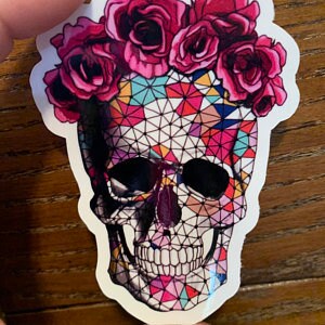 Peut inclure: Un autocollant de cr&acirc;ne g&eacute;om&eacute;trique color&eacute; avec une couronne de roses roses. Le cr&acirc;ne est soulign&eacute; de noir et a un fond blanc.