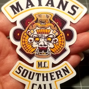May include: White and yellow motorcycle club patch with the words "Mayans M.C. Southern Cali." and a stylized image of a Mayan god's face.