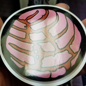 Peut inclure: Un autocollant rond en forme de concha, de couleur rose et marron, avec une finition brillante. L'autocollant pr&eacute;sente un design d&eacute;taill&eacute; d'un pain sucr&eacute; mexicain traditionnel.