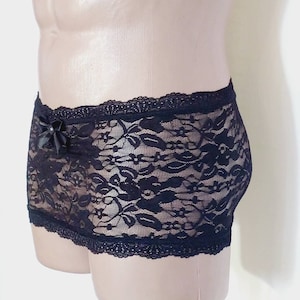 May include: Black lace underwear with a bow detail. The underwear has a floral pattern and is made of a sheer fabric.