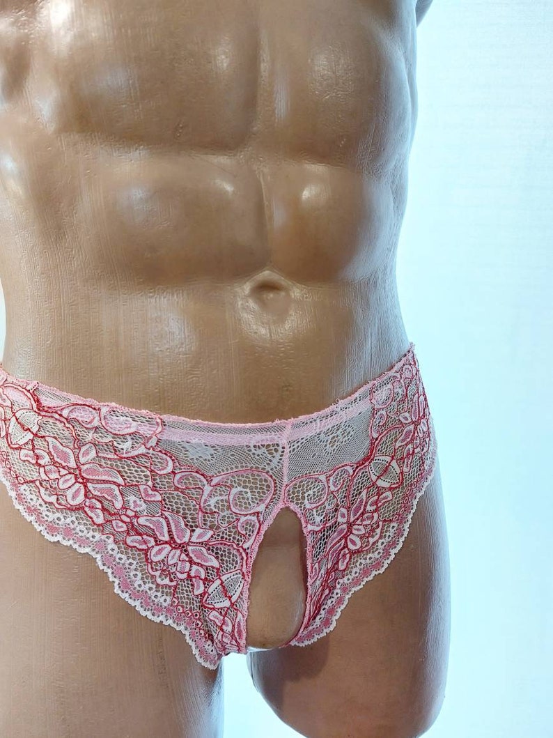 May include: Pink lace underwear with a floral design and a keyhole front. The underwear features a delicate, openwork pattern with red accents and a scalloped edge. The garment is displayed on a mannequin.