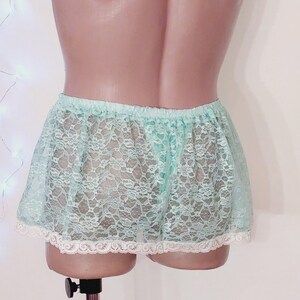 Puede incluir: Una falda de encaje verde claro con un ribete de encaje blanco. La falda es transparente y tiene un delicado patr&oacute;n floral.