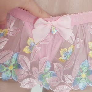 May include: Pink sheer lingerie with floral embroidery and a pink satin bow with a rhinestone embellishment.