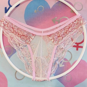 May include: Pink and white lace underwear with a delicate floral pattern. The underwear is sheer and has a pink ribbon trim.