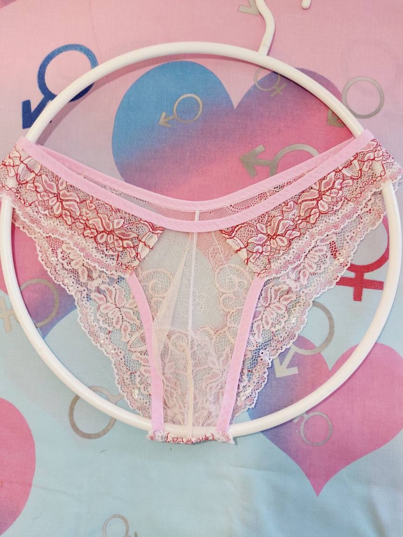 May include: Pink and white lace underwear with a delicate floral pattern. The underwear is sheer and has a pink ribbon trim.