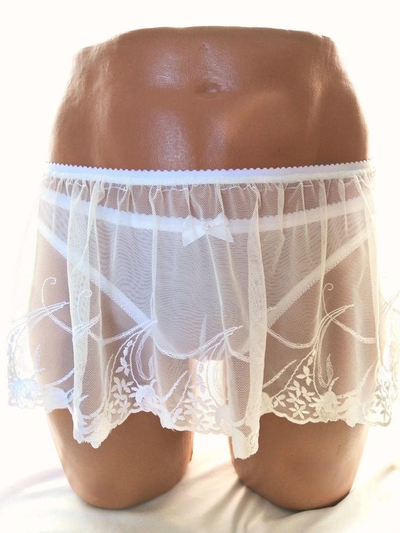 May include: White lace skirt with a delicate floral pattern. The skirt is sheer and has a ruffled hem.