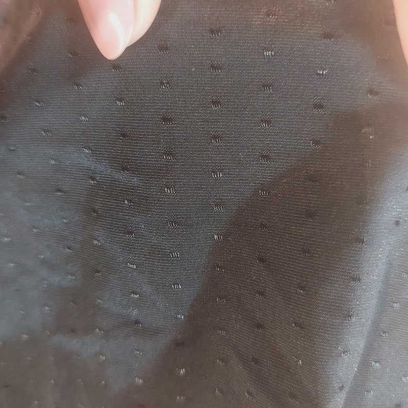 Puede incluir: Primer plano de una tela negra con un patr&oacute;n texturizado de puntos. La tela tiene una superficie lisa y ligeramente brillante.
