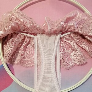 Pu&ograve; includere: Intimo in pizzo rosa con fodera in rete bianca. L'intimo &egrave; appeso a un appendiabiti bianco.