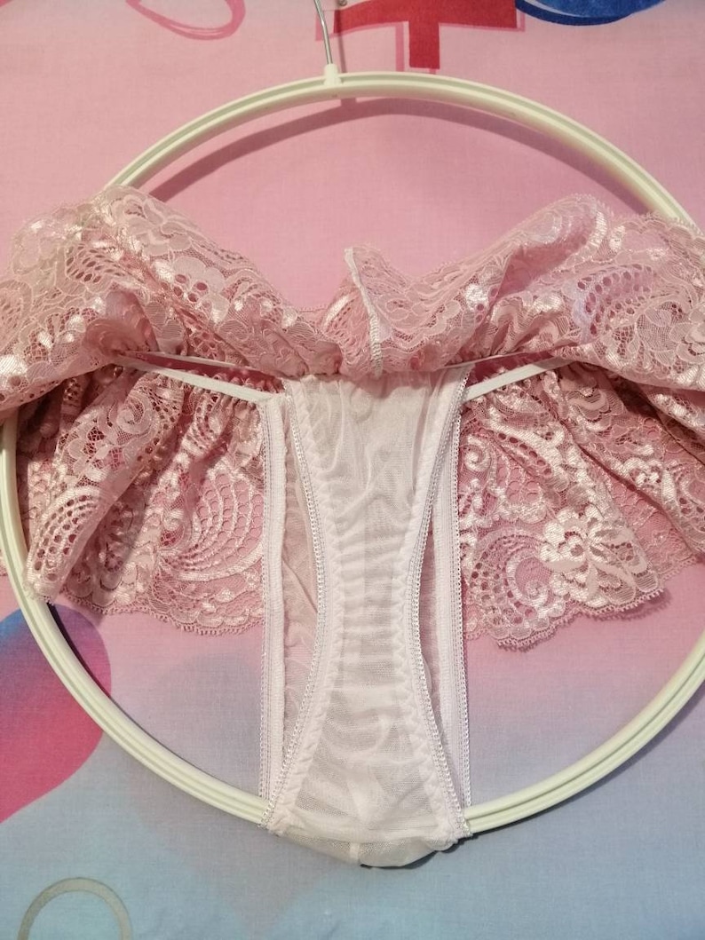 Pu&ograve; includere: Intimo in pizzo rosa con fodera in rete bianca. L'intimo &egrave; appeso a un appendiabiti bianco.