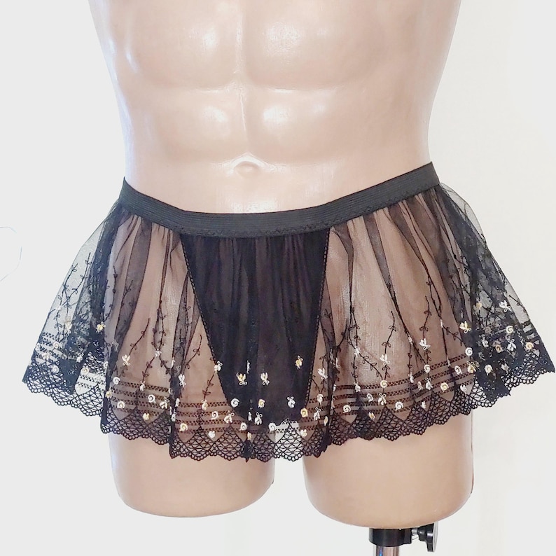 May include: Black sheer skirt with a delicate floral pattern and scalloped lace trim. The skirt has a black elastic waistband and a layered design. The skirt is designed to be worn as lingerie or a costume.