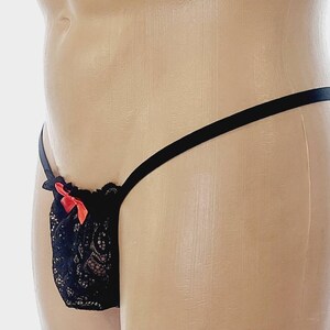 May include: Black lace underwear with a red bow. The underwear has a thin black strap that goes around the waist and ties at the back.
