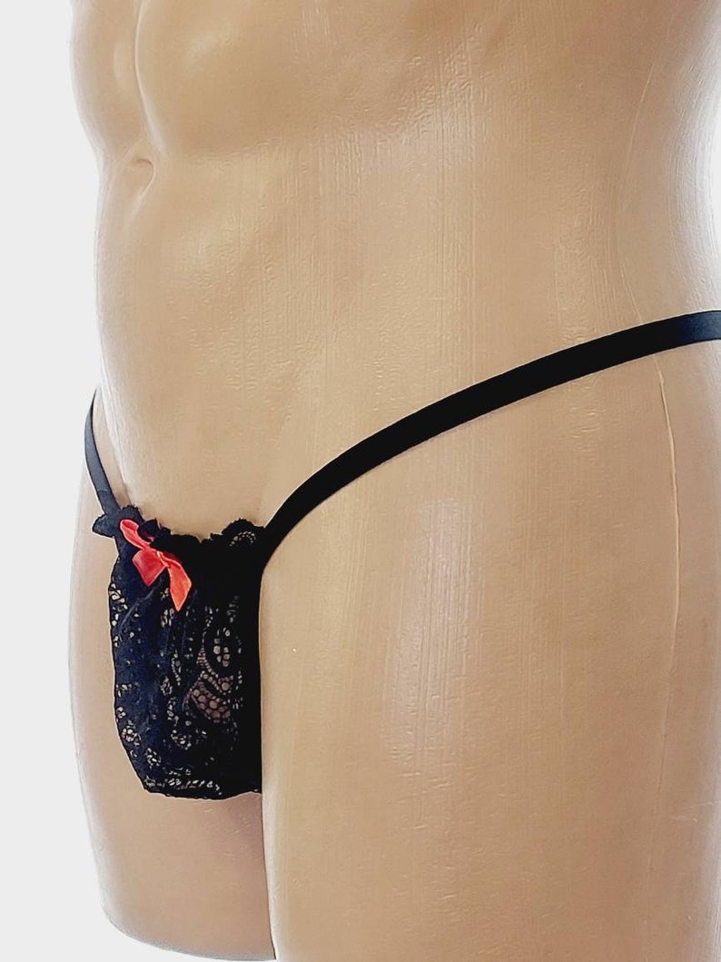 May include: Black lace underwear with a red bow. The underwear has a thin black strap that goes around the waist and ties at the back.