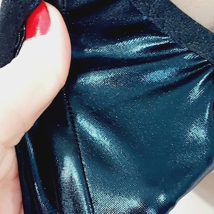 Könnte beinhalten: Nahaufnahme eines blaugrünen Stoffes mit einem schwarzen Gummiband oben. Der Stoff hat eine glänzende, metallische Oberfläche.