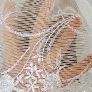 May include: White lace fabric with a delicate floral pattern. The lace is sheer and has a soft, flowing texture.