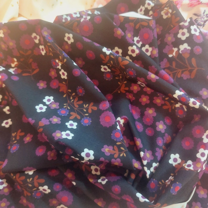 Puede incluir: Tela negra con un patr&oacute;n floral blanco y morado. La tela est&aacute; doblada y texturizada.