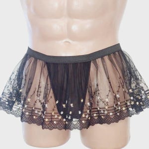 May include: Black sheer skirt with an elastic waistband. The skirt features a delicate floral pattern with gold accents and a scalloped lace trim along the hemline. The skirt is designed with a layered, flared silhouette.