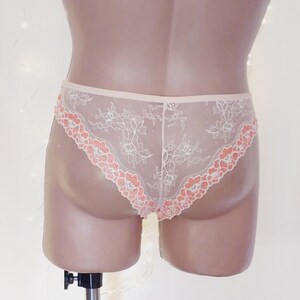 Puede incluir: Ropa interior de encaje blanco con un ribete floral de color melocot&oacute;n. La ropa interior es transparente y tiene un delicado patr&oacute;n floral.