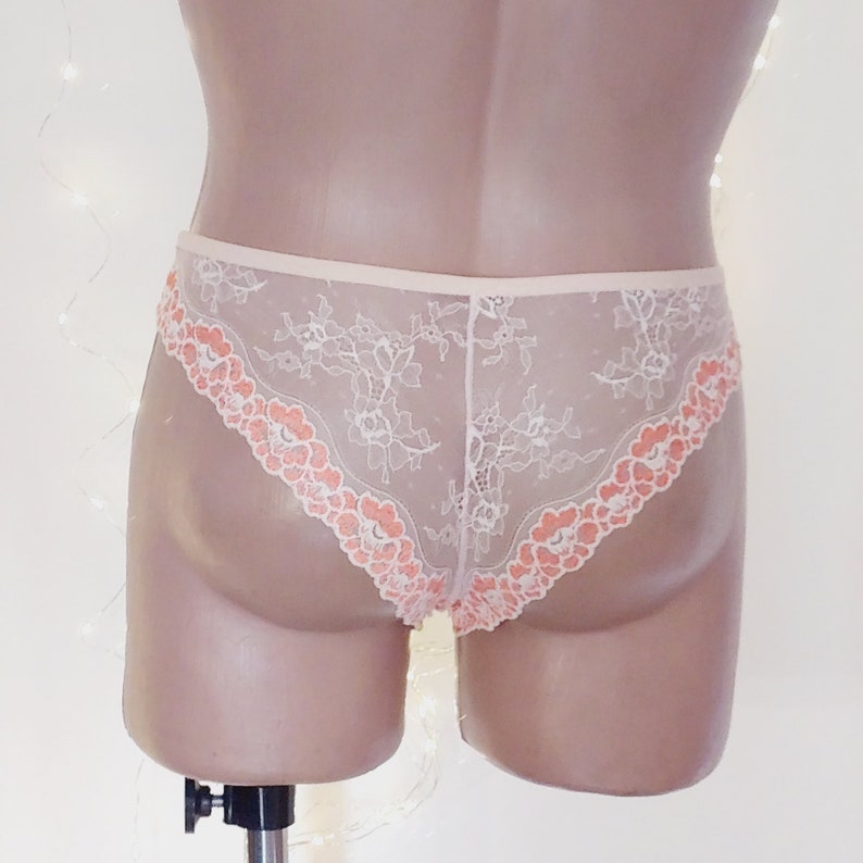 Puede incluir: Ropa interior de encaje blanco con un ribete floral de color melocot&oacute;n. La ropa interior es transparente y tiene un delicado patr&oacute;n floral.