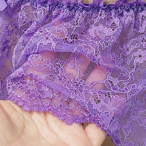Puede incluir: Tela de encaje morado con un delicado patrón floral. El encaje tiene un borde rizado.