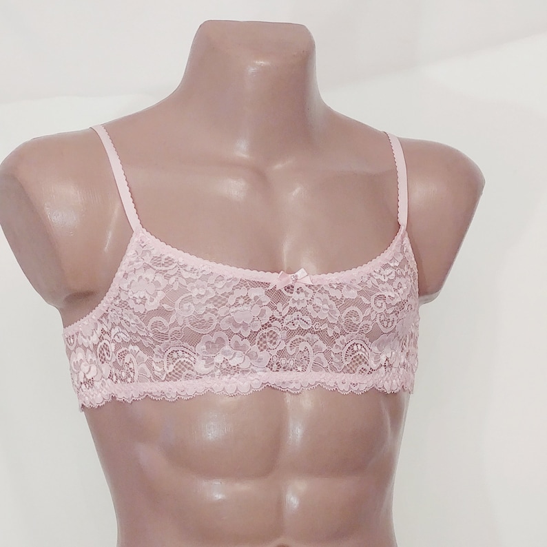 May include: A pink lace bralette with adjustable straps. The bralette features a delicate floral pattern and a bow in the centre.