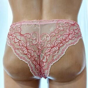 May include: Pink and red lace underwear with a floral design. The underwear features a delicate, intricate pattern and a scalloped edge. The garment is displayed on a mannequin.