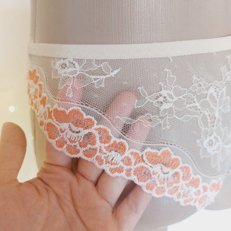Puede incluir: Ropa interior de encaje blanco con un patr&oacute;n floral de color melocot&oacute;n.
