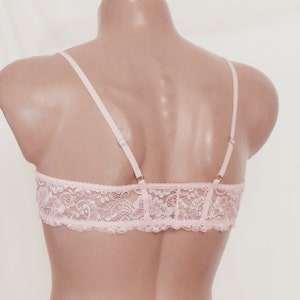 May include: A pink lace bralette with adjustable straps. The bralette is made of delicate lace and has a soft, feminine look.