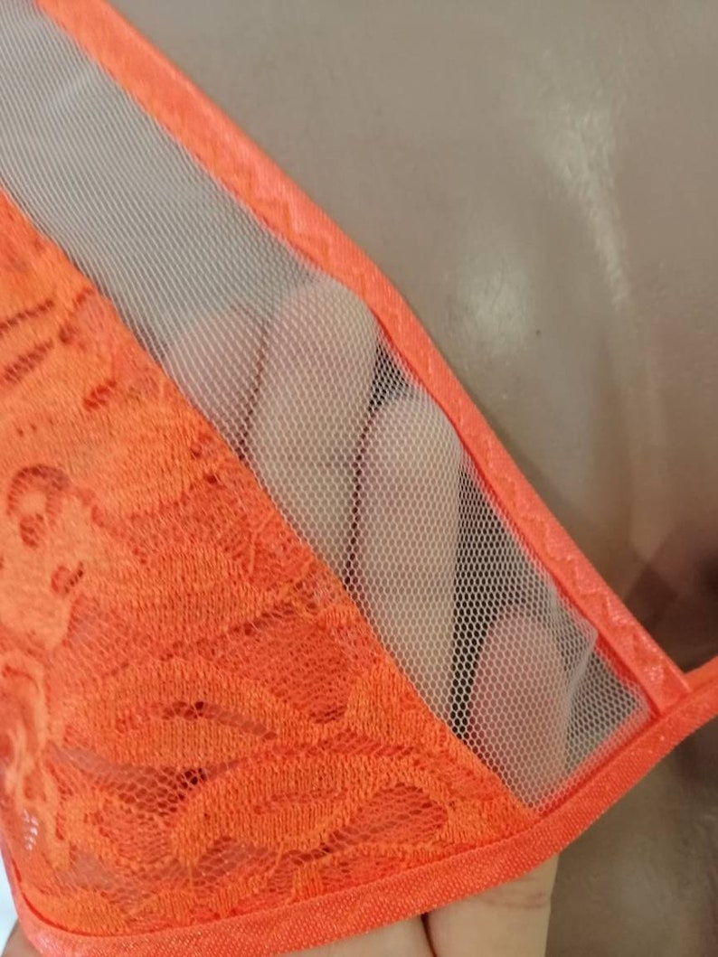 May include: Orange lace fabric with a sheer mesh panel. The lace has a delicate floral pattern.