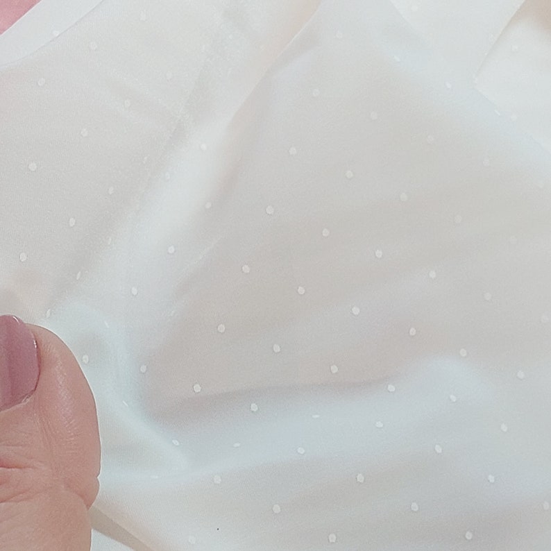 Puede incluir: Tela blanca con un sutil patr&oacute;n de lunares blancos. La tela es lisa y tiene un ligero brillo.
