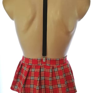 Puede incluir: Una minifalda roja y negra a cuadros con una tira de tirantes negra. La falda es plisada y tiene una cintura ajustada.