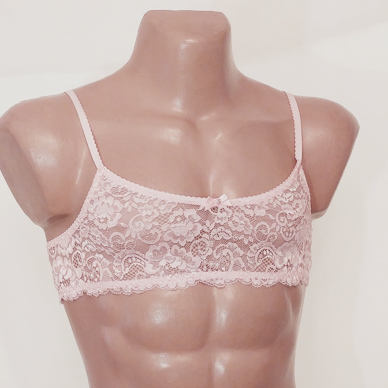 May include: A pink lace bralette with adjustable straps. The bralette features a delicate floral pattern and a bow detail in the centre.
