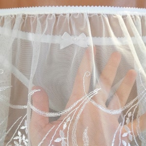 May include: White lace trim with a delicate floral pattern. The lace is soft and sheer, with a ruffled edge.
