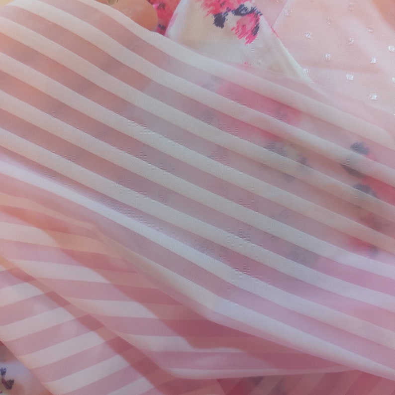 Puede incluir: Tela rosa transparente con rayas blancas. La tela est&aacute; doblada y tiene una textura suave y delicada.