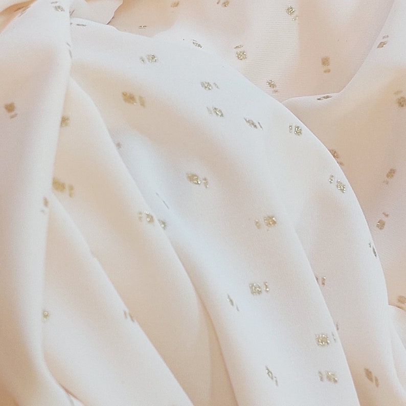 Puede incluir: Tela blanca con un sutil patr&oacute;n de puntos dorados. La tela es suave y tiene un ligero brillo.