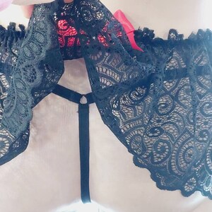 May include: Black lace underwear with a red bow. The underwear has a delicate floral pattern and a thin black strap.