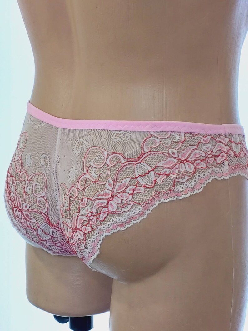 May include: Pink and white lace underwear with a delicate floral pattern. The underwear has a pink elastic waistband.