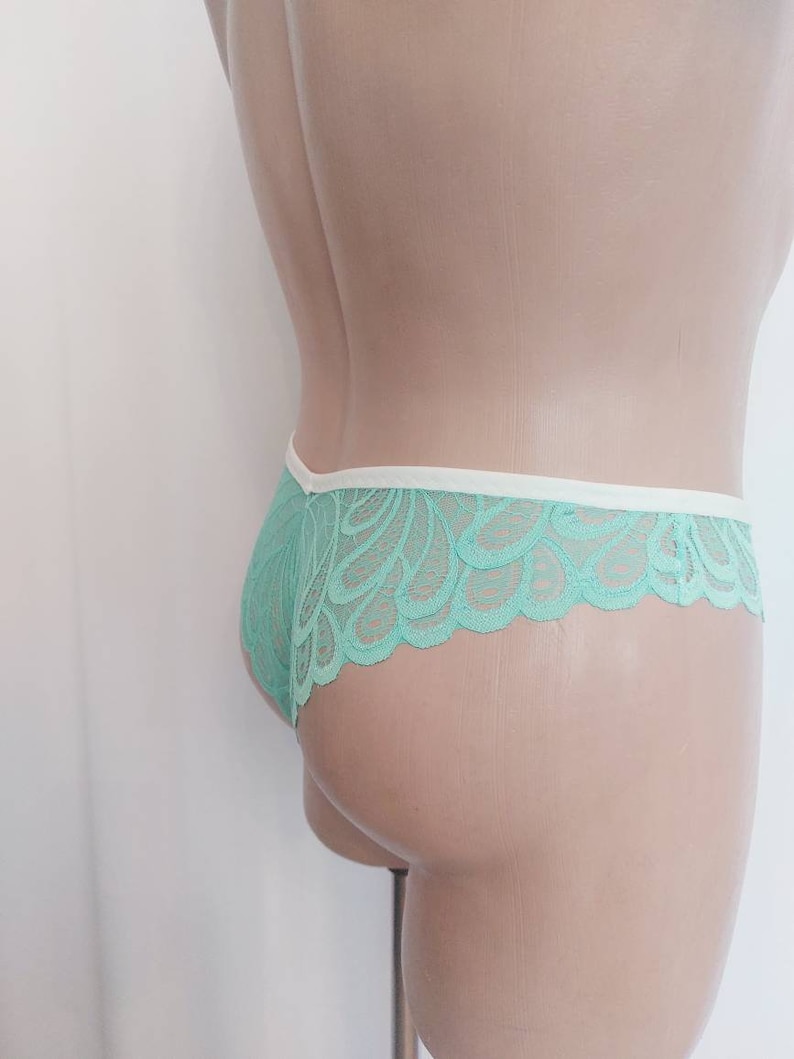 May include: Mint green lace underwear with a white trim. The underwear is shown on a mannequin.