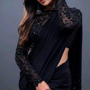 Puede incluir: Una mujer lleva un sari negro con bordados intrincados y un anillo de plata. El sari está drapeado en un estilo tradicional y el cabello de la mujer está peinado en ondas sueltas.