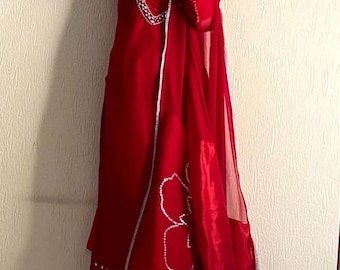 Könnte beinhalten: Ein rotes, langärmeliges Kleid mit weißem Besatz und einem Blumendesign auf dem Rock. Das Kleid wird mit einer passenden roten Hose und einem durchsichtigen roten Schal getragen.