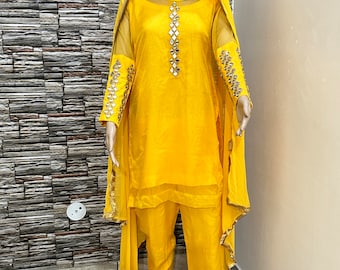 May include: A yellow salwar kameez with a sheer dupatta. The kameez has a round neckline and is decorated with mirror work. The salwar is also yellow and has a straight cut. The dupatta is sheer and has a gold border.