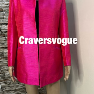 Pode incluir: Um blazer rosa brilhante com gola mandarim e mangas compridas. O blazer tem um brilho sutil e uma silhueta ligeiramente ajustada. O texto "Craversvogue" é visível na frente do blazer.